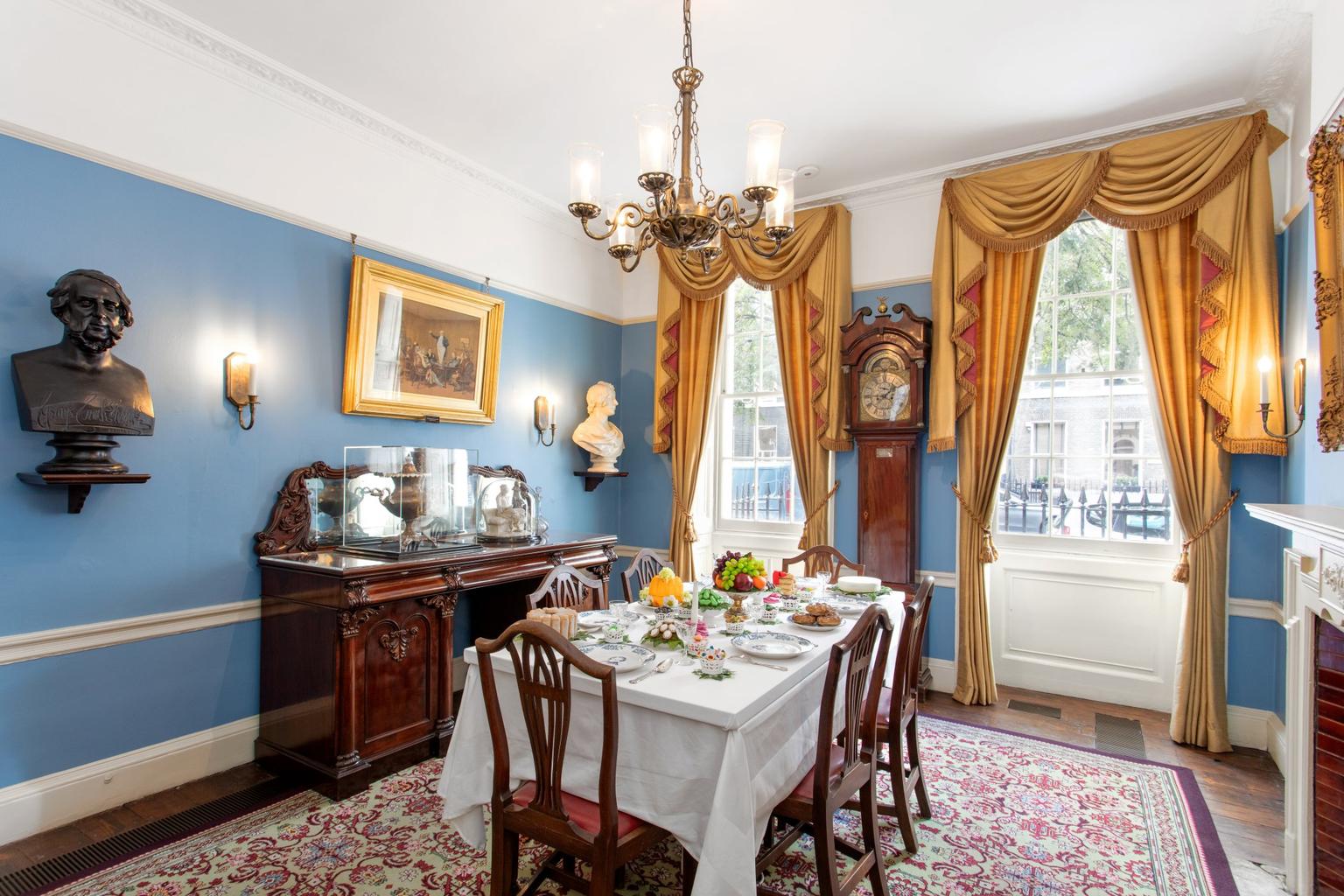 A small blue-walled dining room with gold curtains and antique furniture