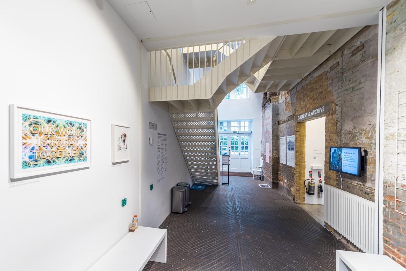 A contemporary gallery space with a brick floor and steel staircase