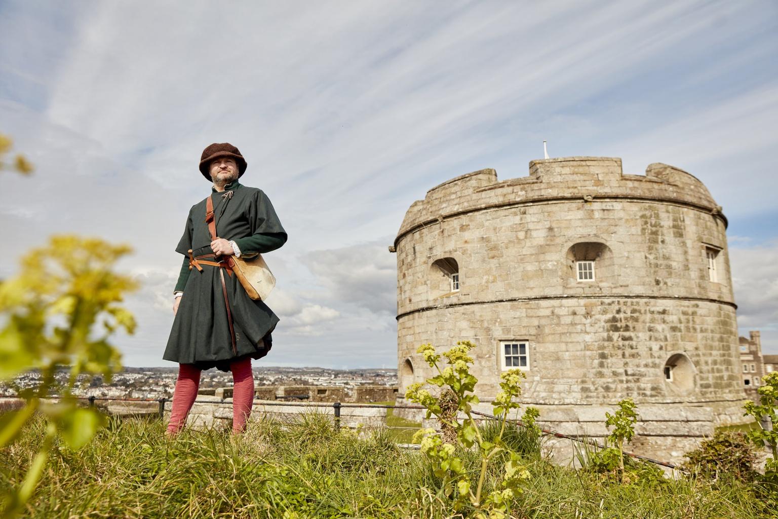 A man in Tudor dress standing in front of a circular castle keep