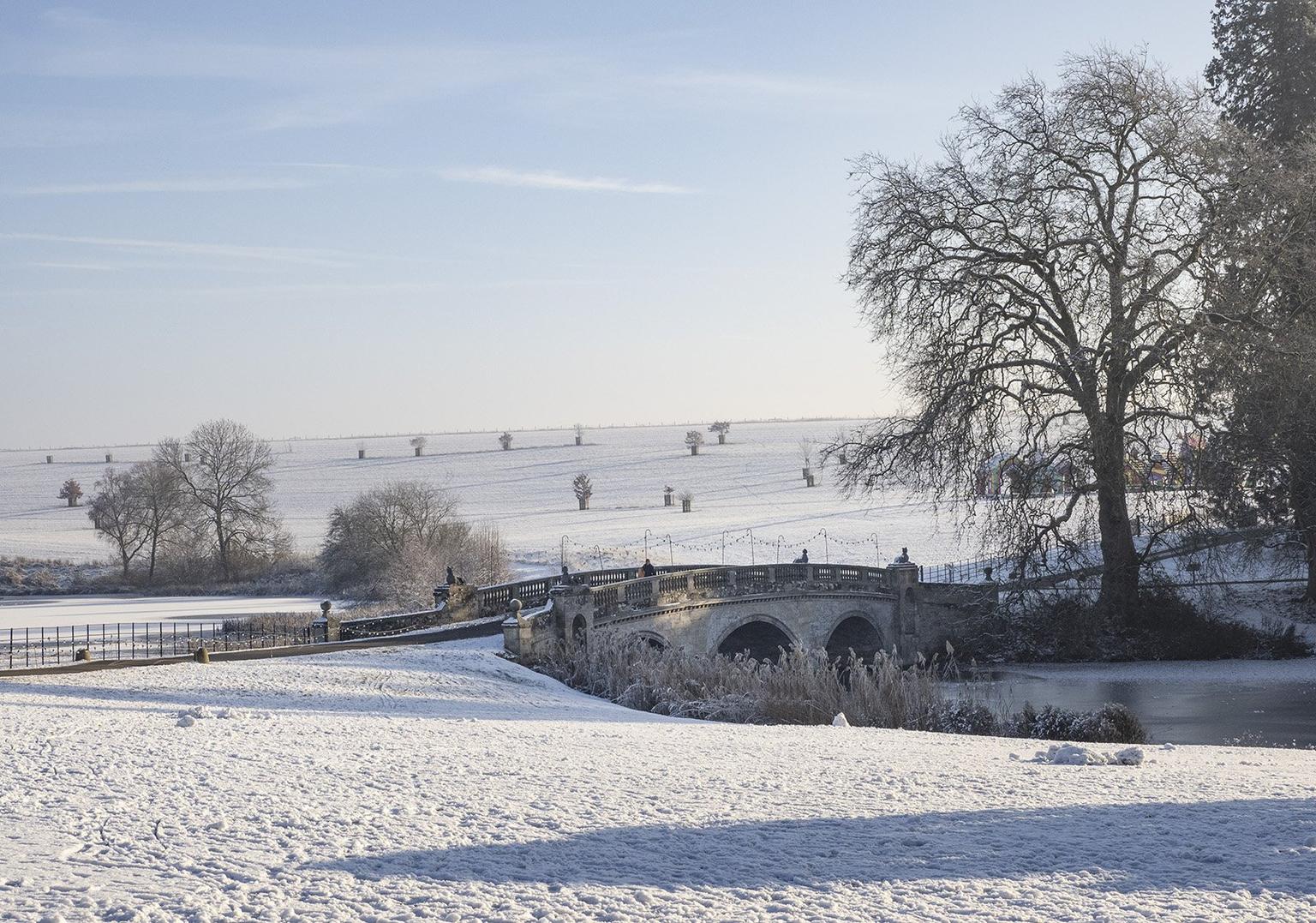 A stone bridge and surrounding fields covered in snow, with leafless trees