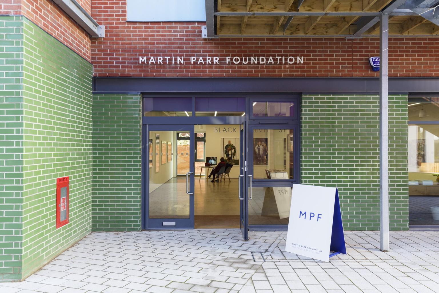 The green brick front of a photography gallery, photographs visible on the walls inside