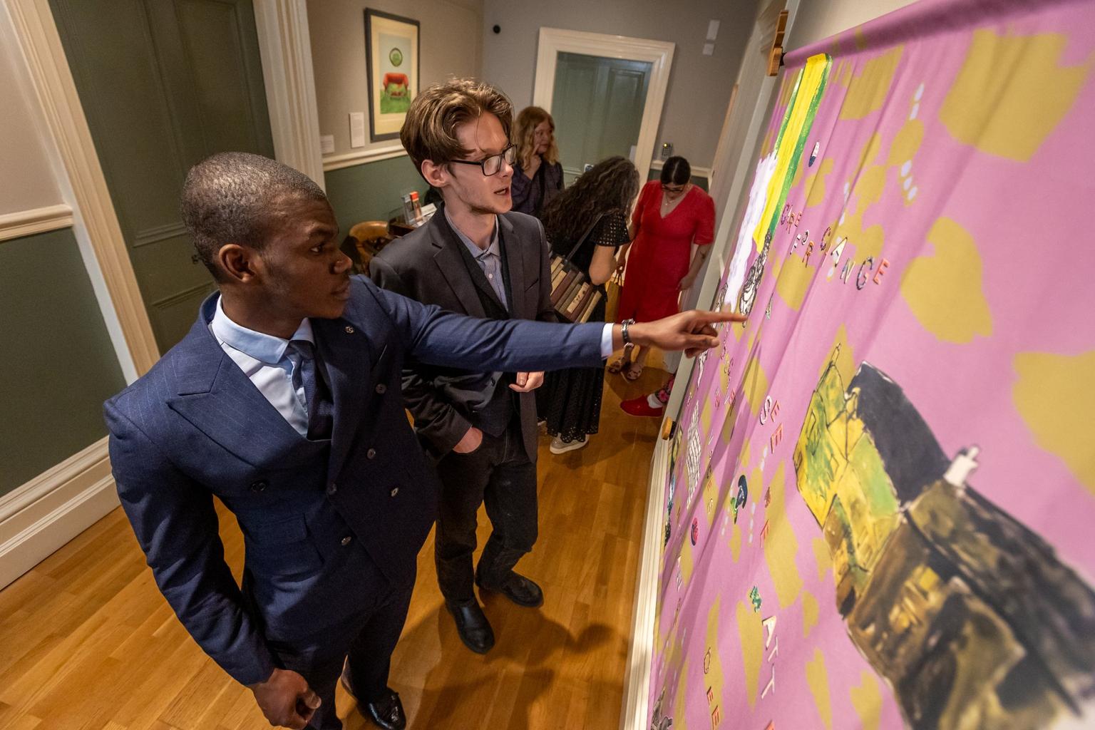 Two men in suits examine and point at a large pink and yellow artwork displayed on a gallery wall.