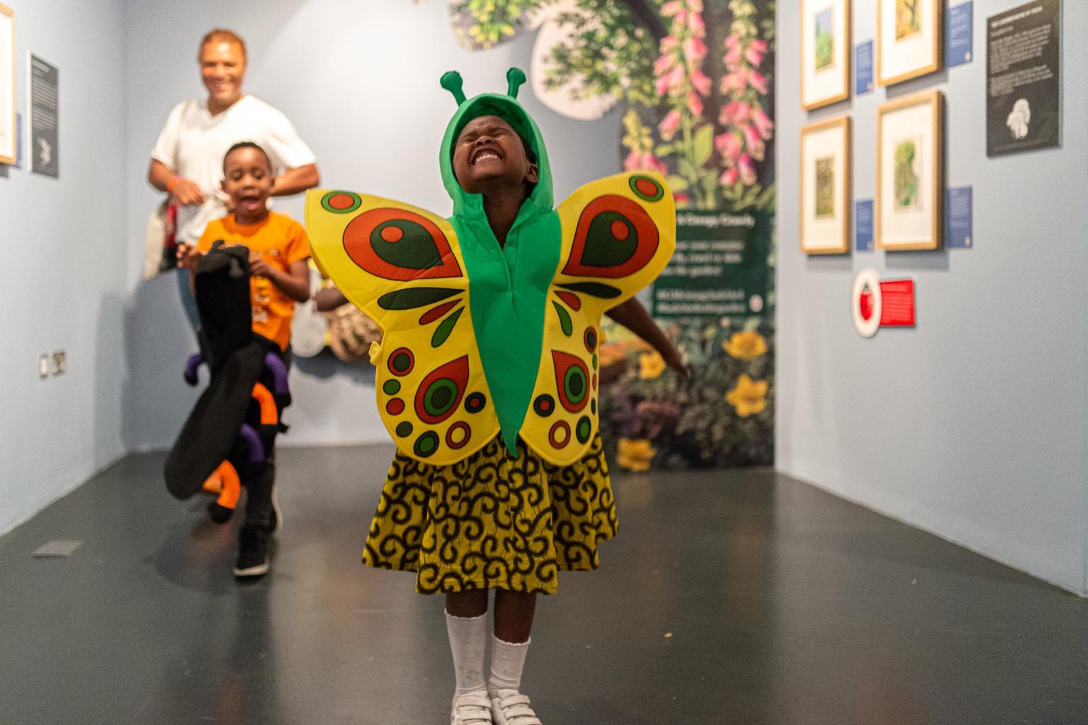 A young child stands in a gallery, excited and dressed in a butterfly costume