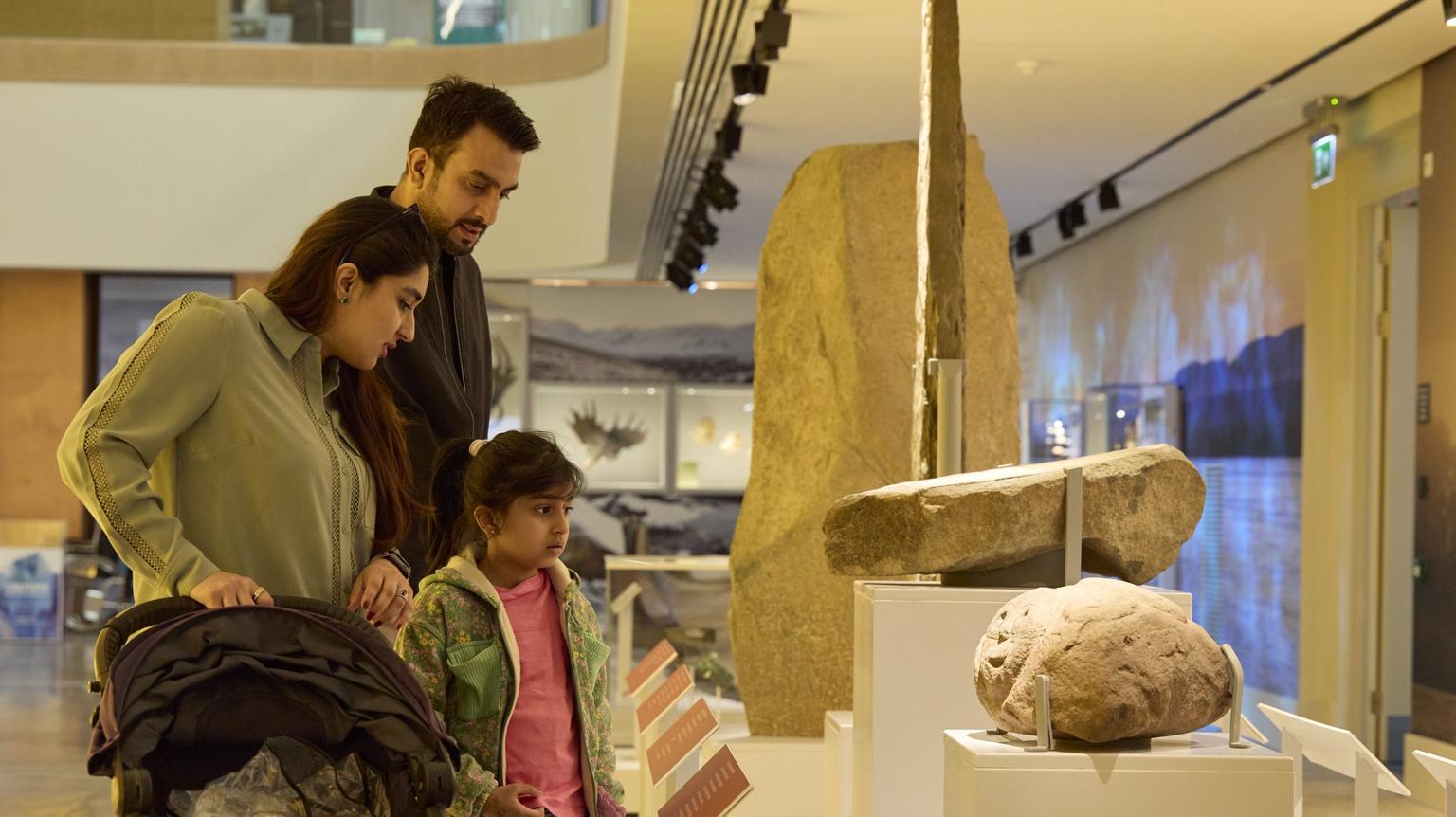 A family of three look at a display of a large beige stone.