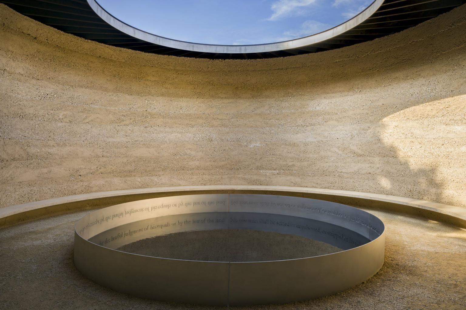 A circular space with a round opening to the sky and round pool of water bordered by an inscription beneath