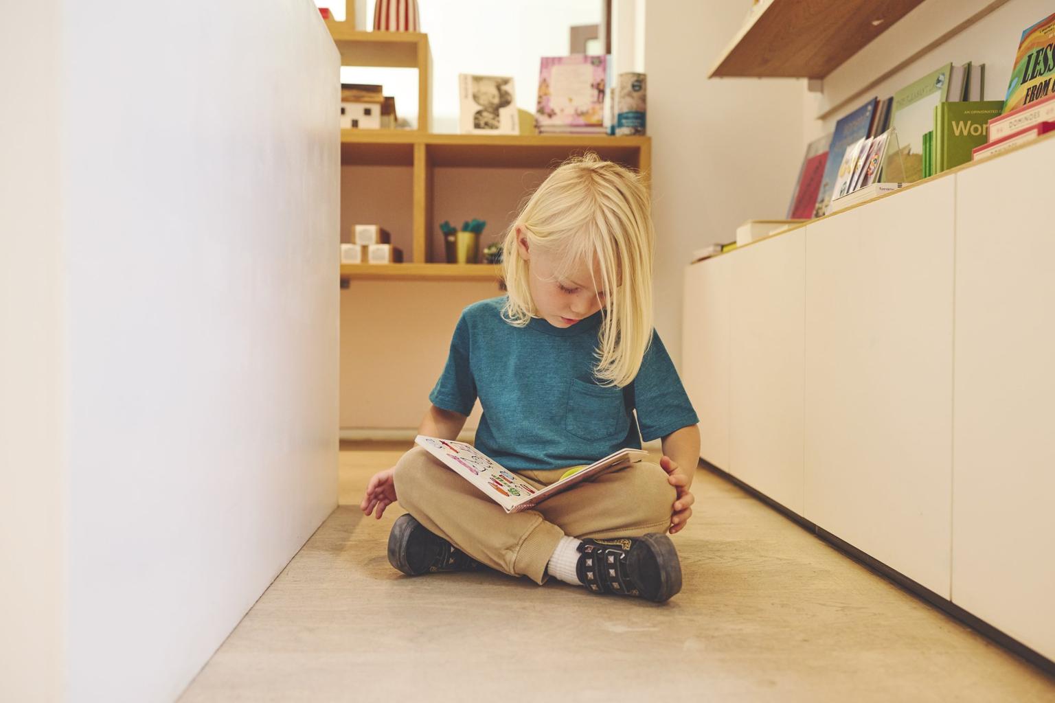 Child sits cross-legged on a library floor reading a colourful picture book.