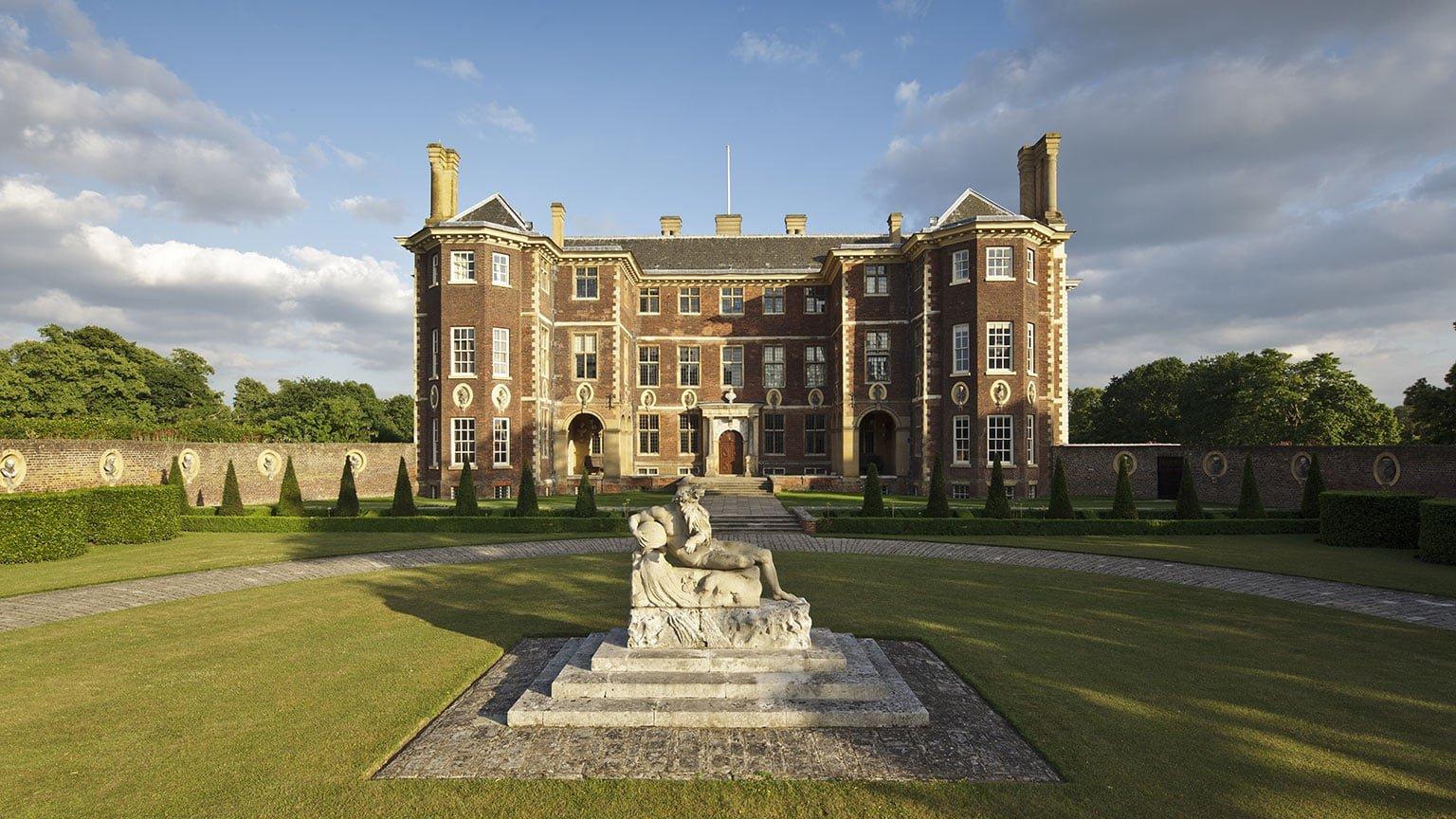 An historic house behind a curved drive, with a stone statue in front