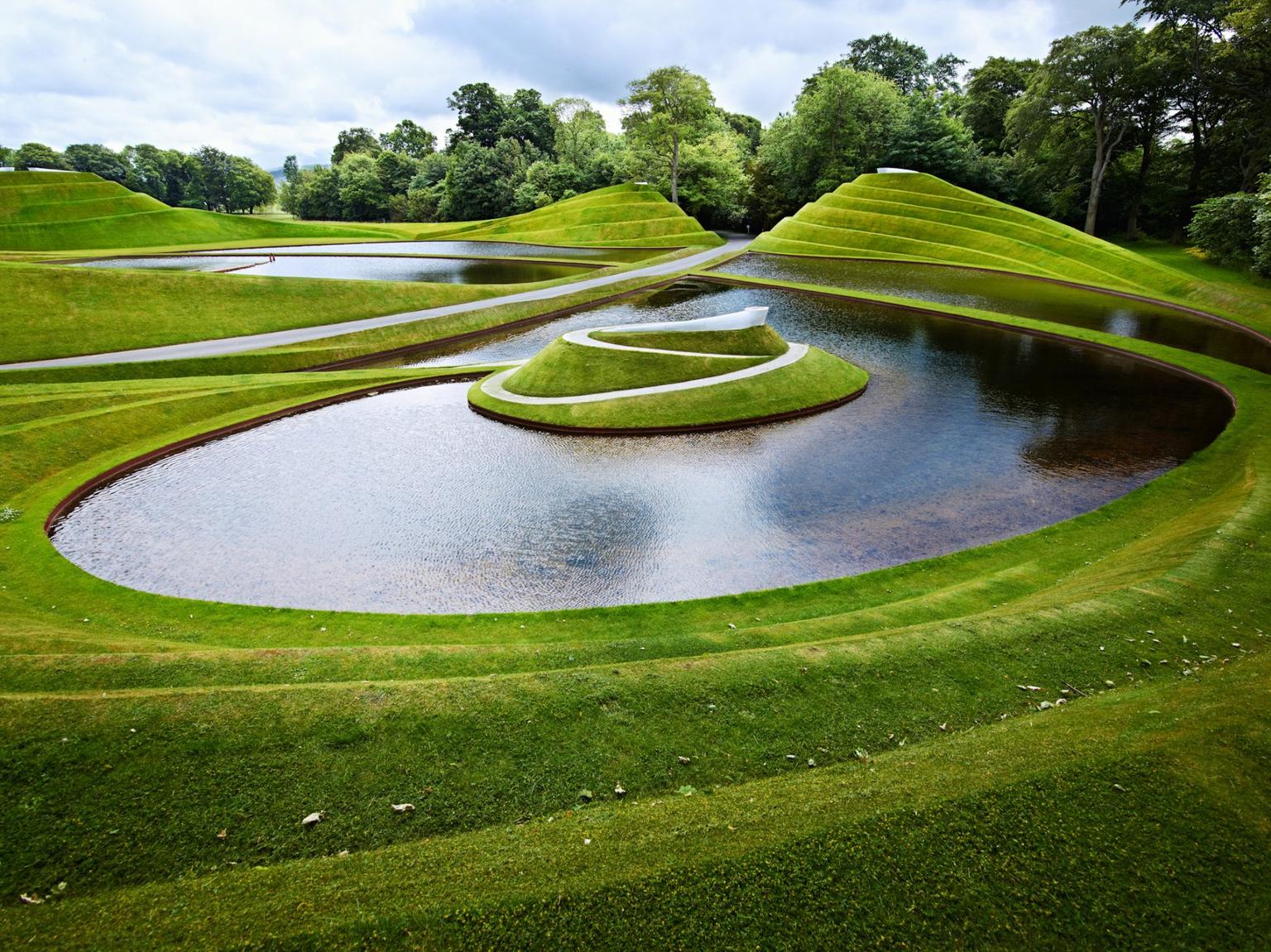 Green turf layered into spirals around pools of water, with trees in the background