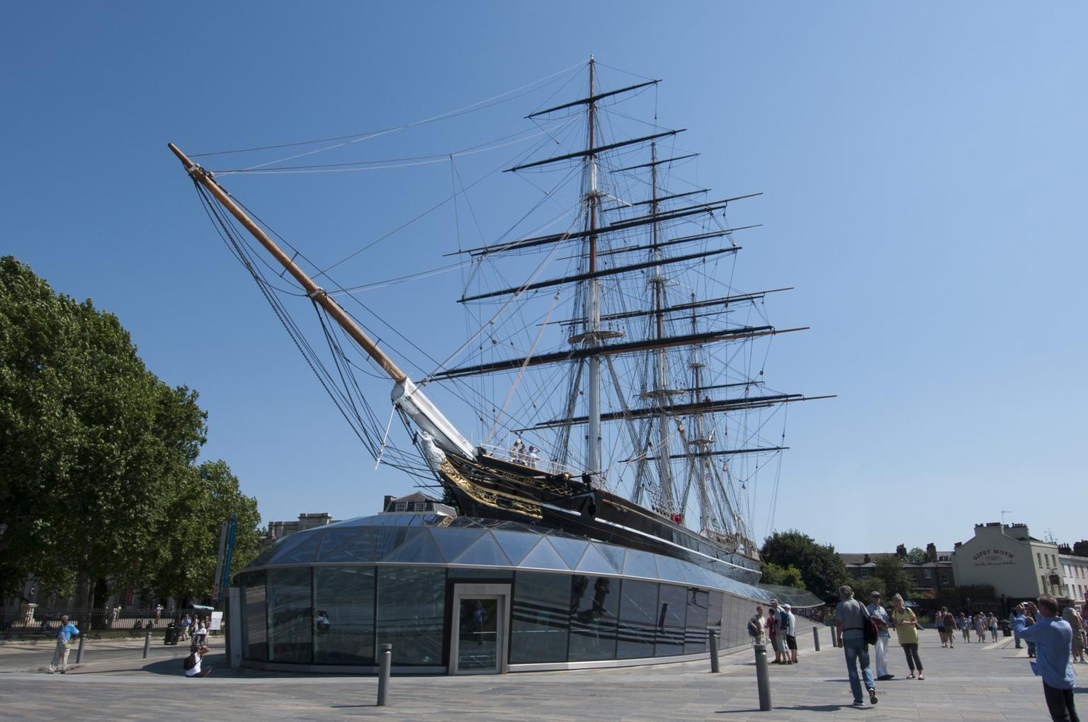 A merchant sailing vessel with exposed masts, placed on land above a glass building.