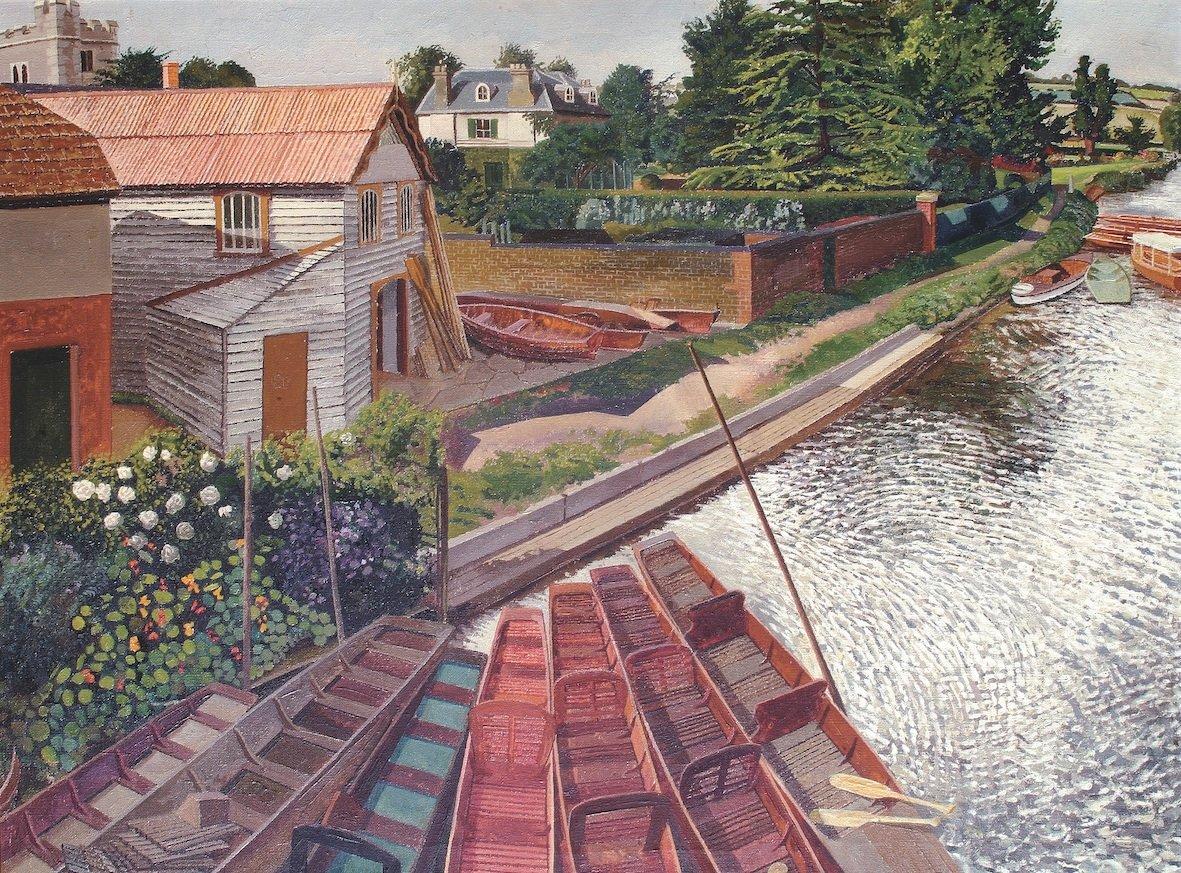 Red and brown rowboats sit moored along a river beside a white wooden boathouse and a flowered garden.