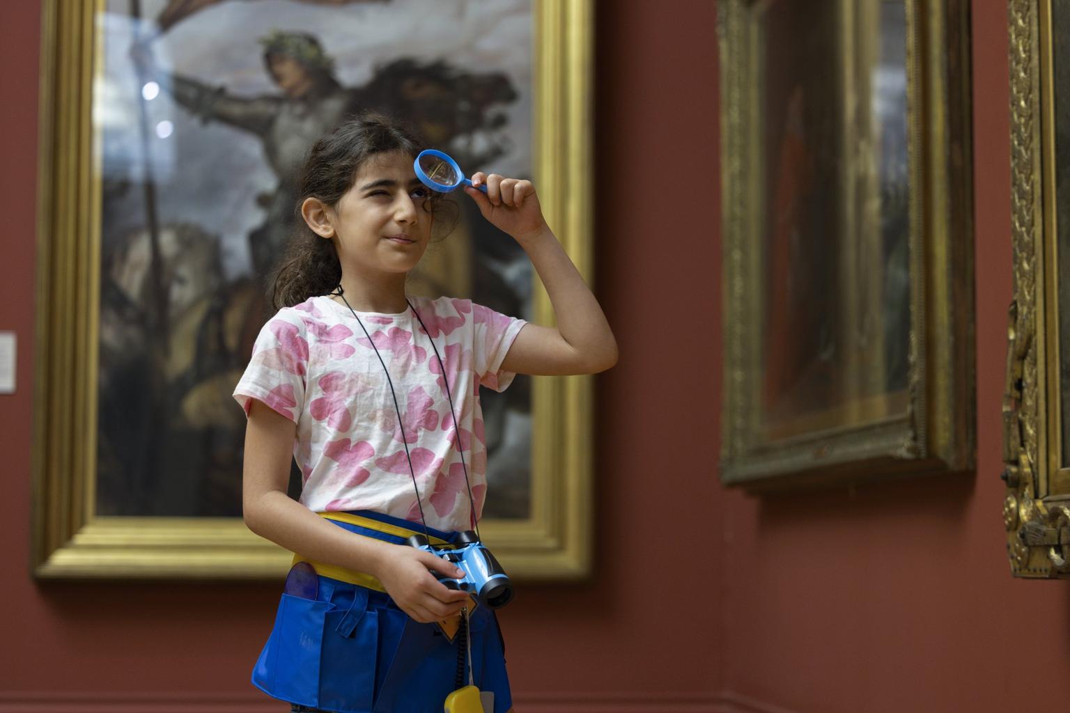 A young girl holds up a magnifying glass to a painting