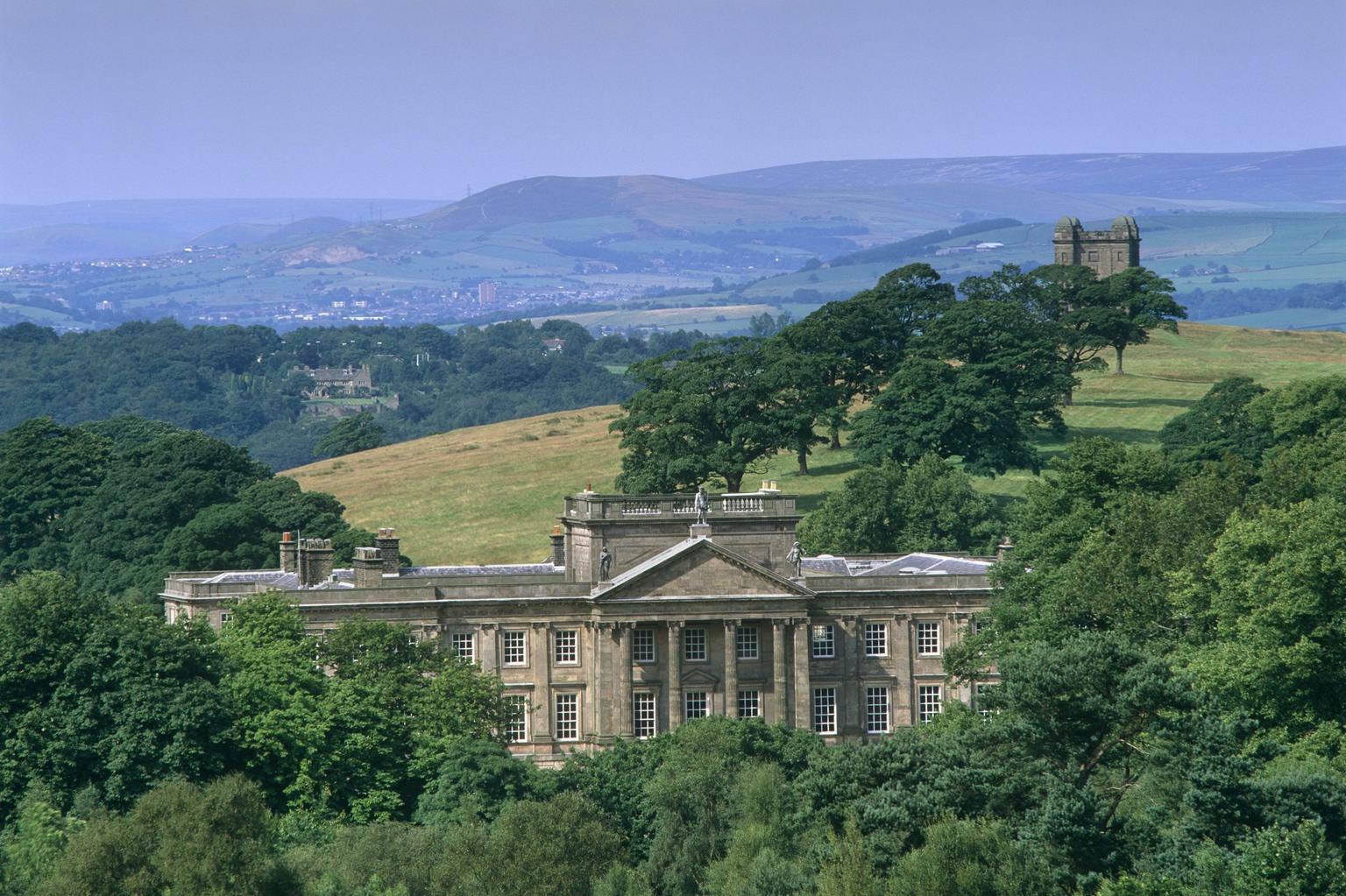 The front of a great hall in the distance, surrounded by trees and with rolling hills beyond