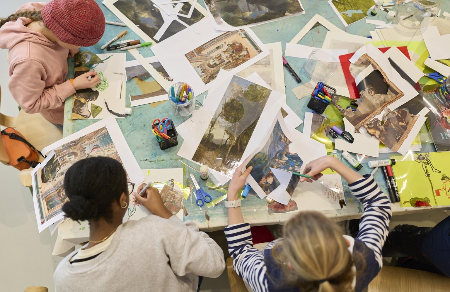 Young visitors sit around a cluttered table cutting and gluing colorful printed images and paper to make a art collages.