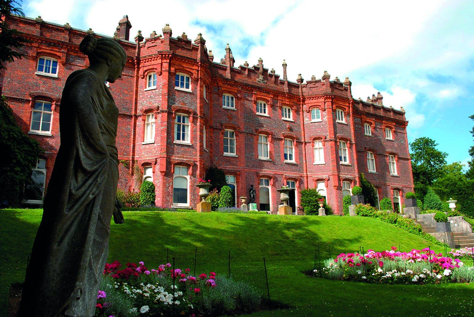 A statue of a woman in front of a manor house, with formal gardens in the foreground