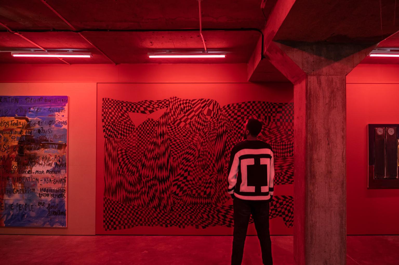 Visitor stands in front of a black and white optical illusion in a room with red lighting