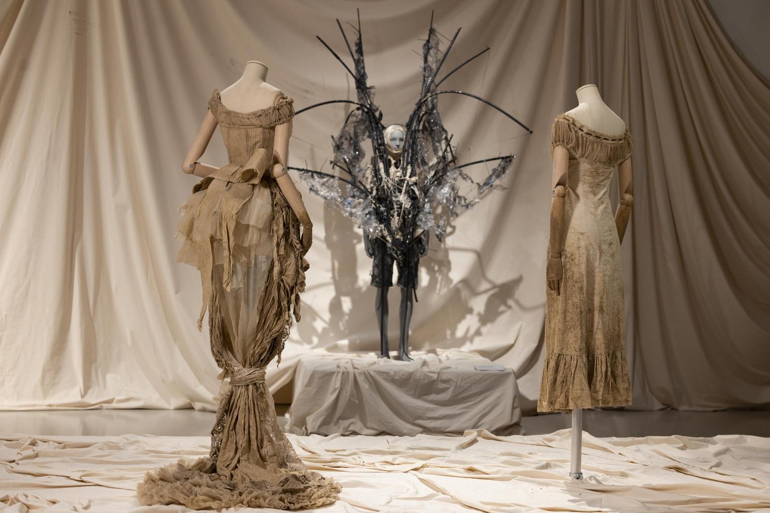 Two mannequins wearing stained dresses in the foreground, a mannequin with wings in the background