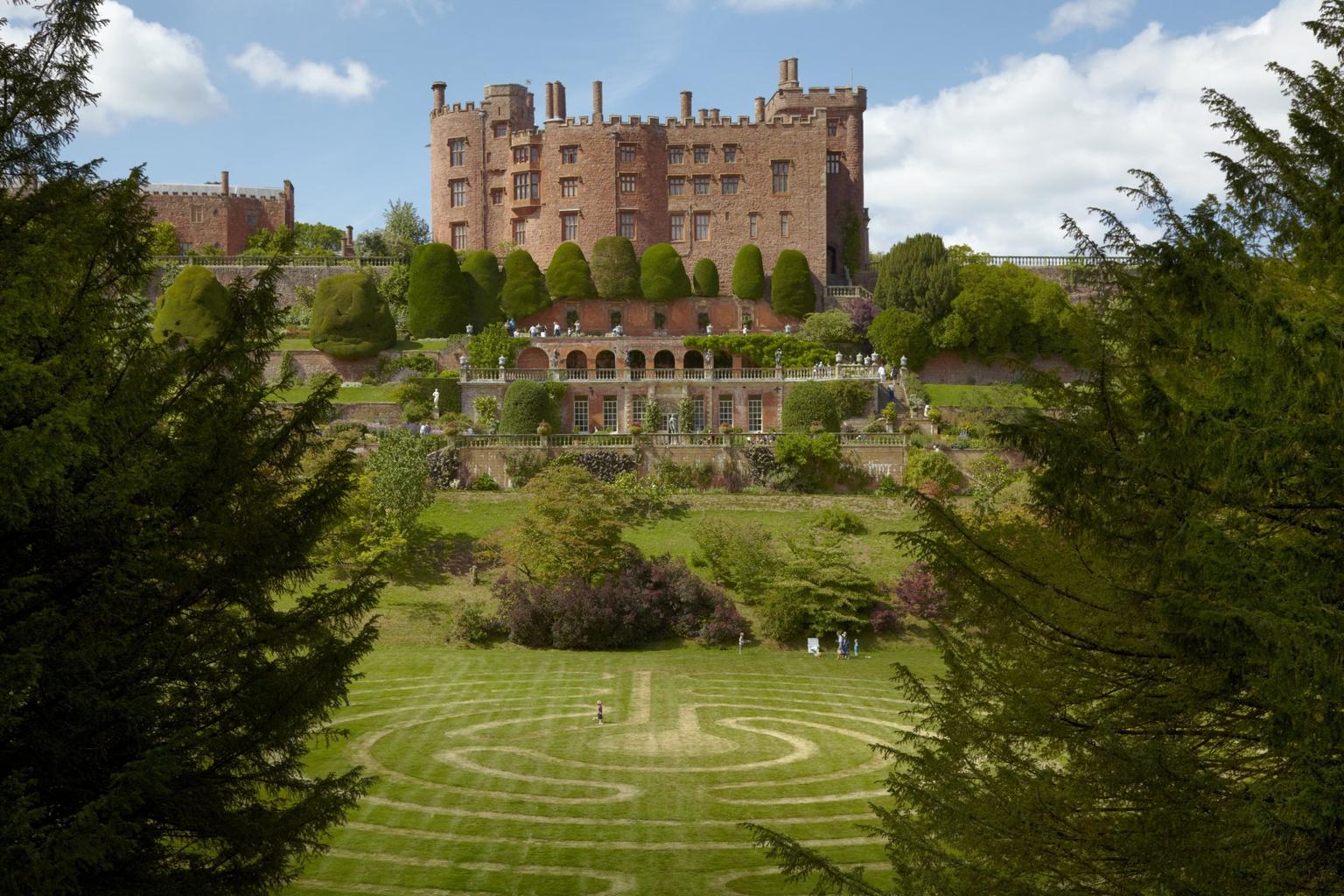 View over a grass maze, ornamental gardens and multi-tiered castle, with trees either side in the foreground