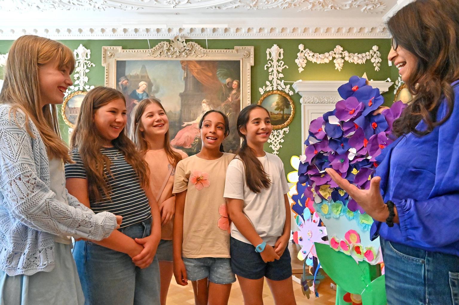 Kids are joined by TV presenter Konnie Huq for the Kids Aloud launch event at the Foundling Museum in London. They are looking at a large purple and blue paper flower display and smiling.
