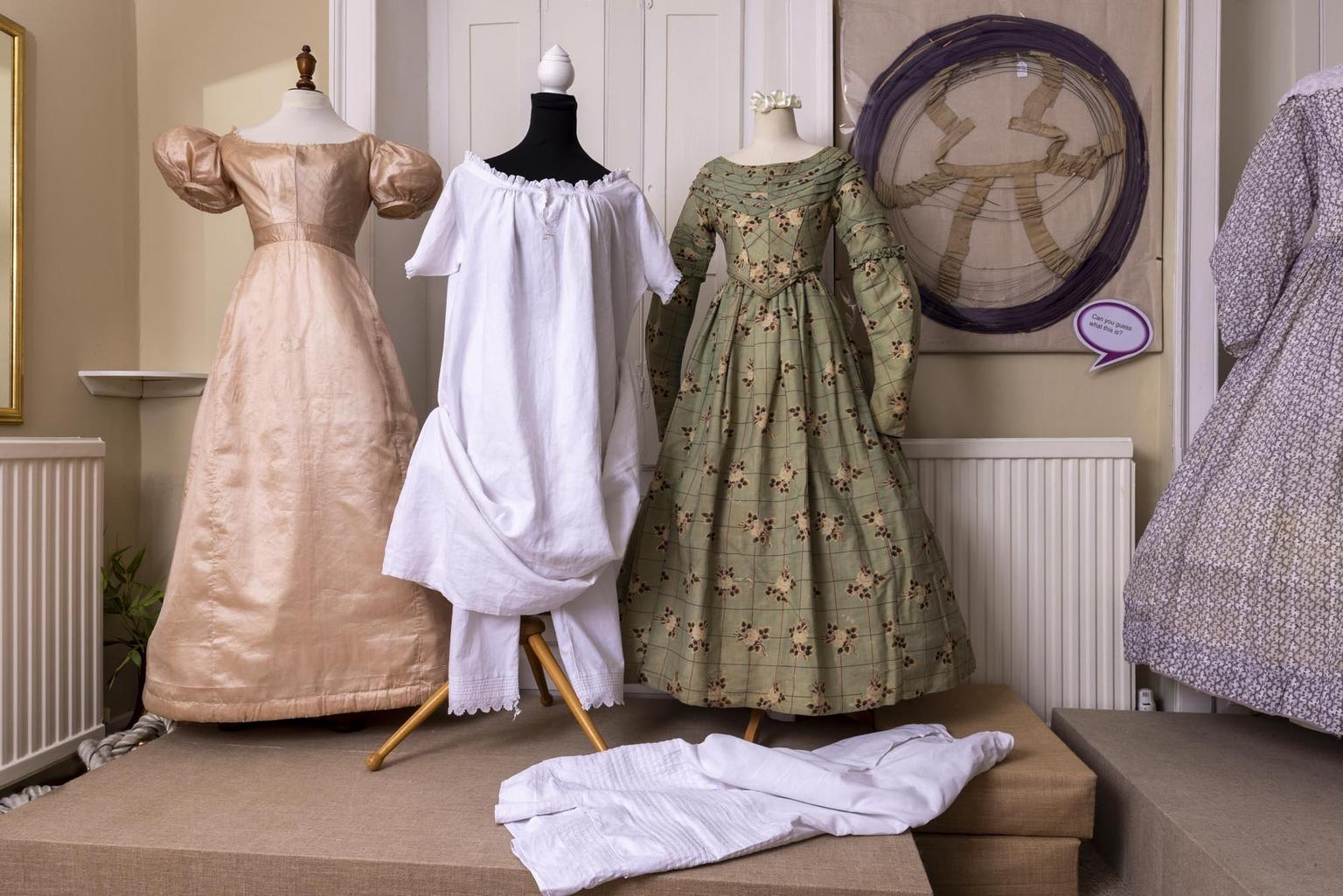 Three mannequins wearing a pink dress, white nightgown and green dress