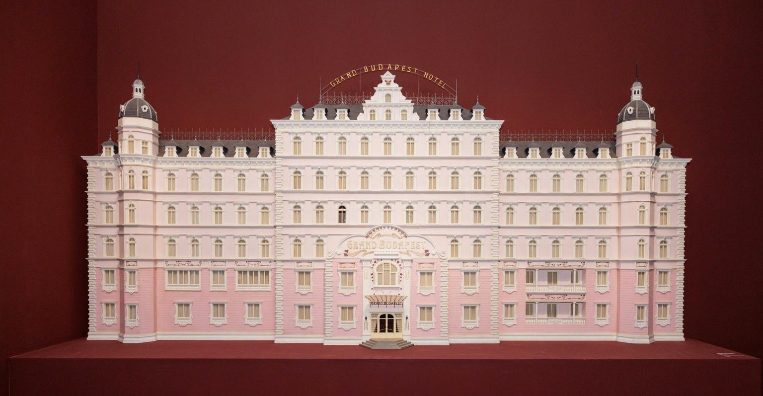 A model of an elaborate, château style pink and white hotel displayed against a dark red background.