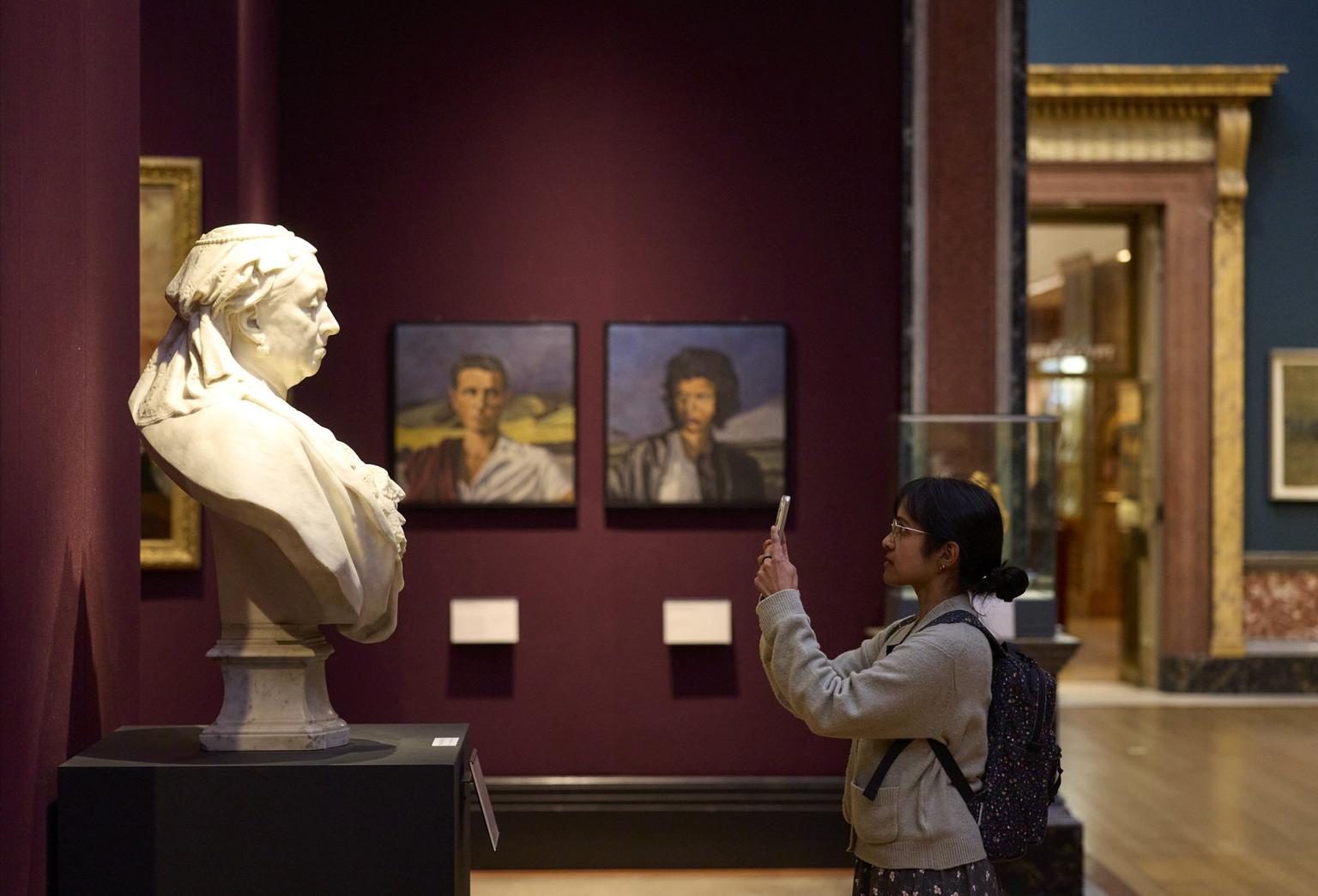 A visitor photographs a white marble bust on their phone.