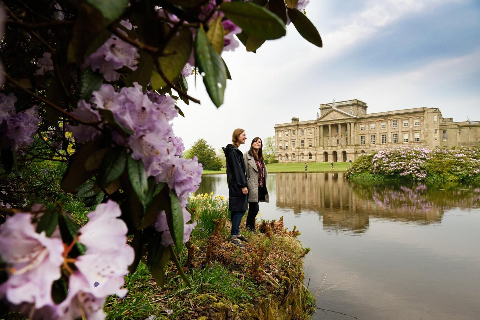 The lake and house at Lyme Park, two women on the shore, pink rhododendron in the foreground