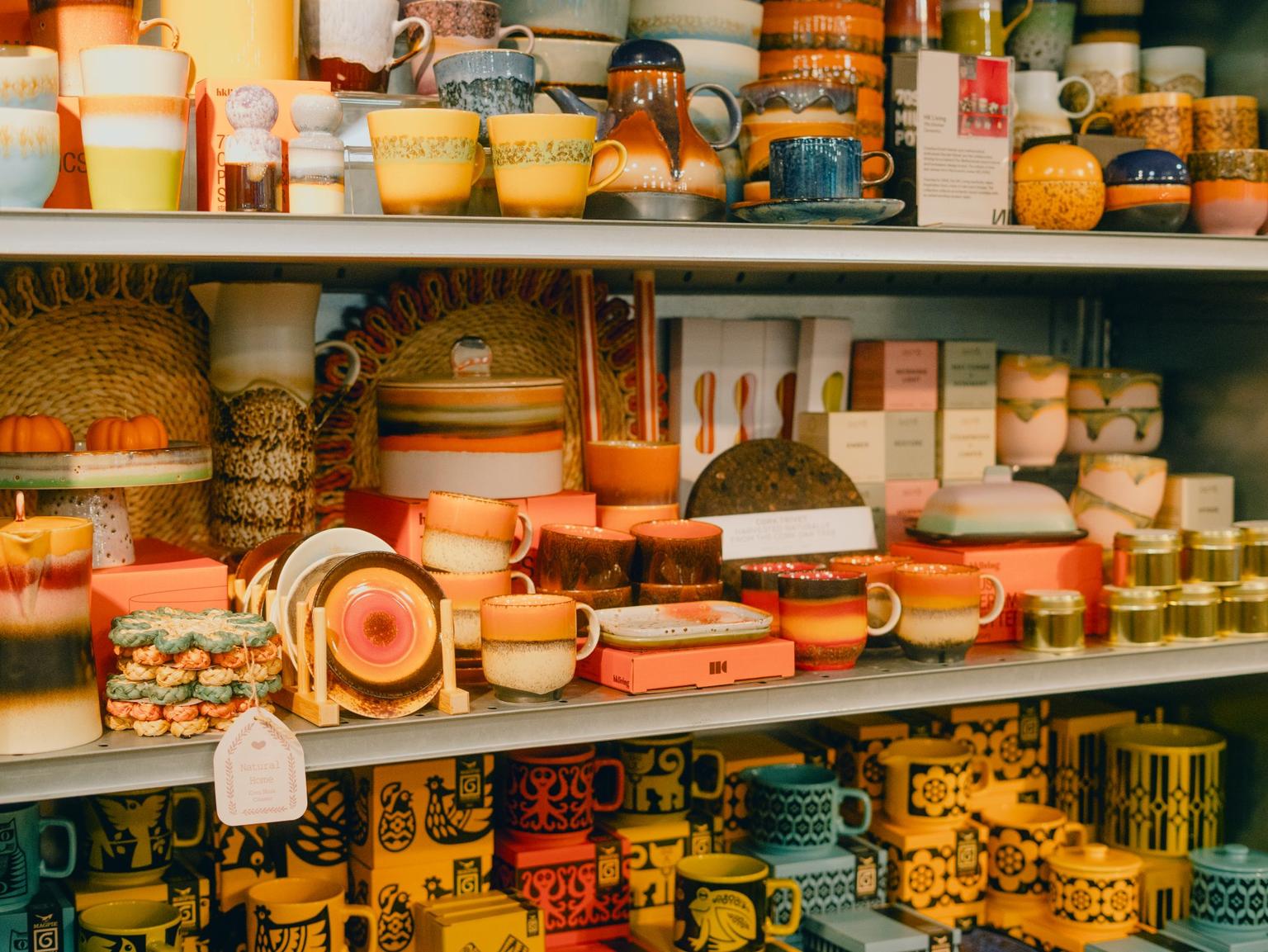Shop shelves stacked with colorful ceramic mugs, cups, plates, and bowls.