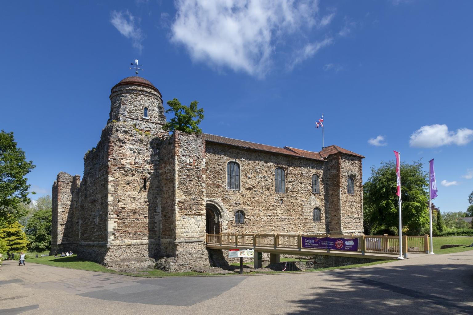 A Norman castle made out of bricks and stone; a modern wooden bridge provides a walkway to its entrance.