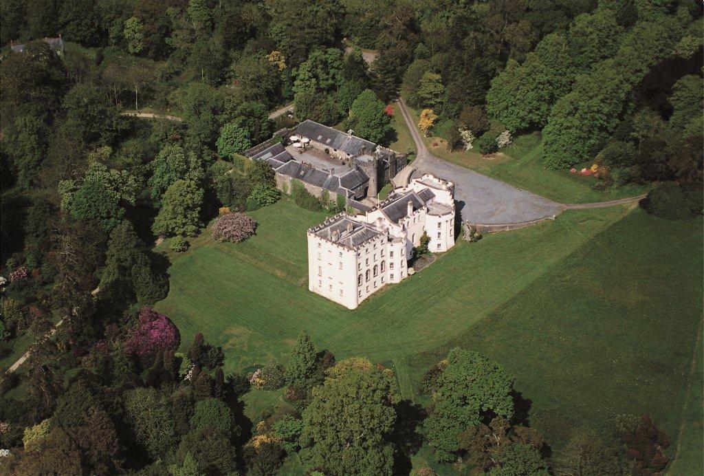 An aerial view of Picton Castle and gardens, featuring a wide expanse of lawn and surrounding trees