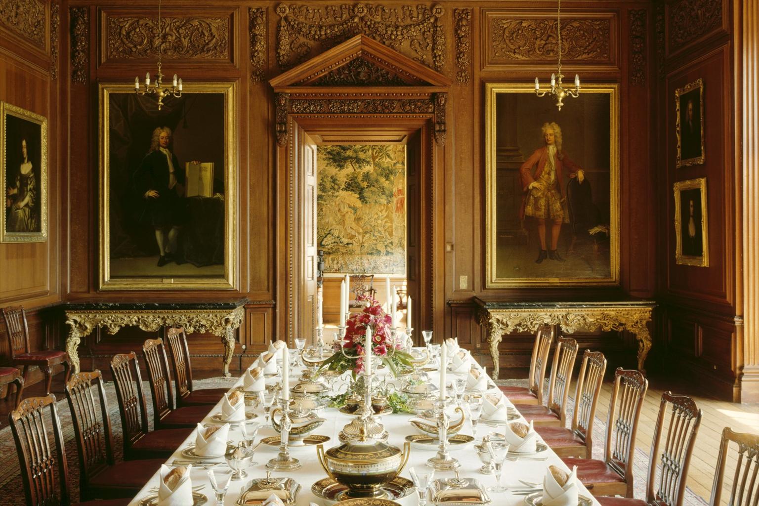 A dining table laid with silver in a wooden panelled room with historic portraits on the walls