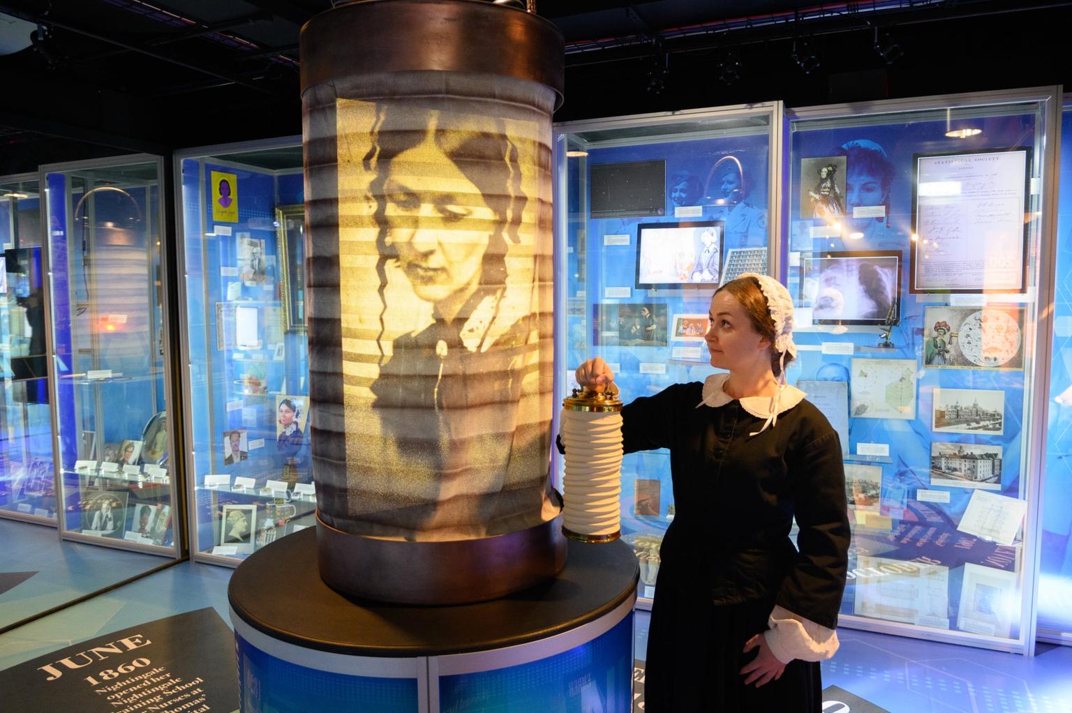 A woman in a period nurse's costume stands in a Florence Nightingale exhibition holding a lamp