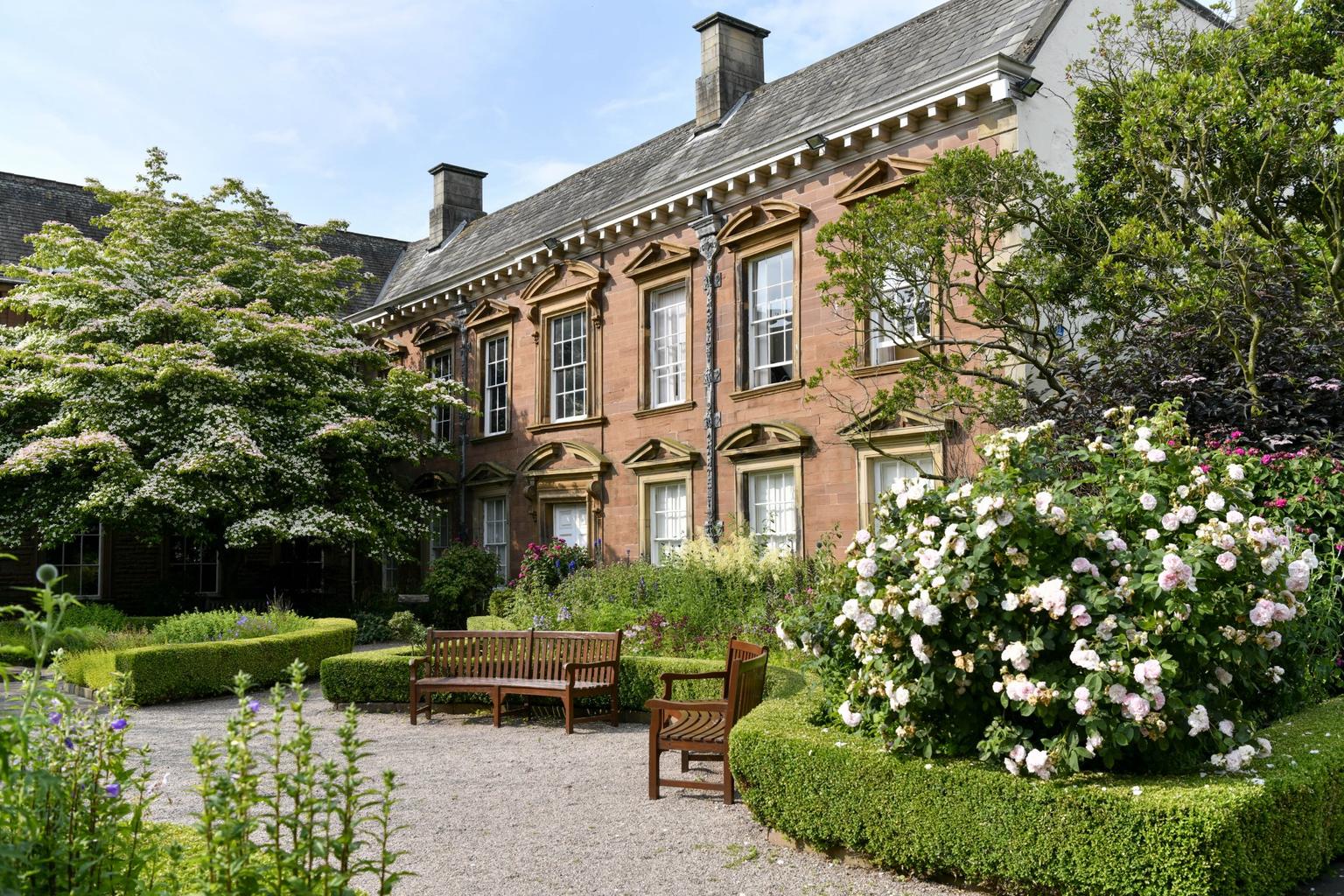 A grand house fronted by flowering trees and shrubs